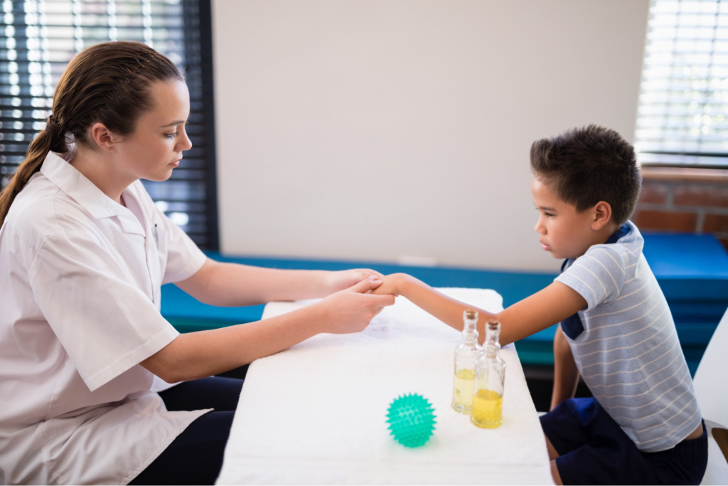 An occupational therapist gently massages a child’s hand using oil during a sensory therapy session.