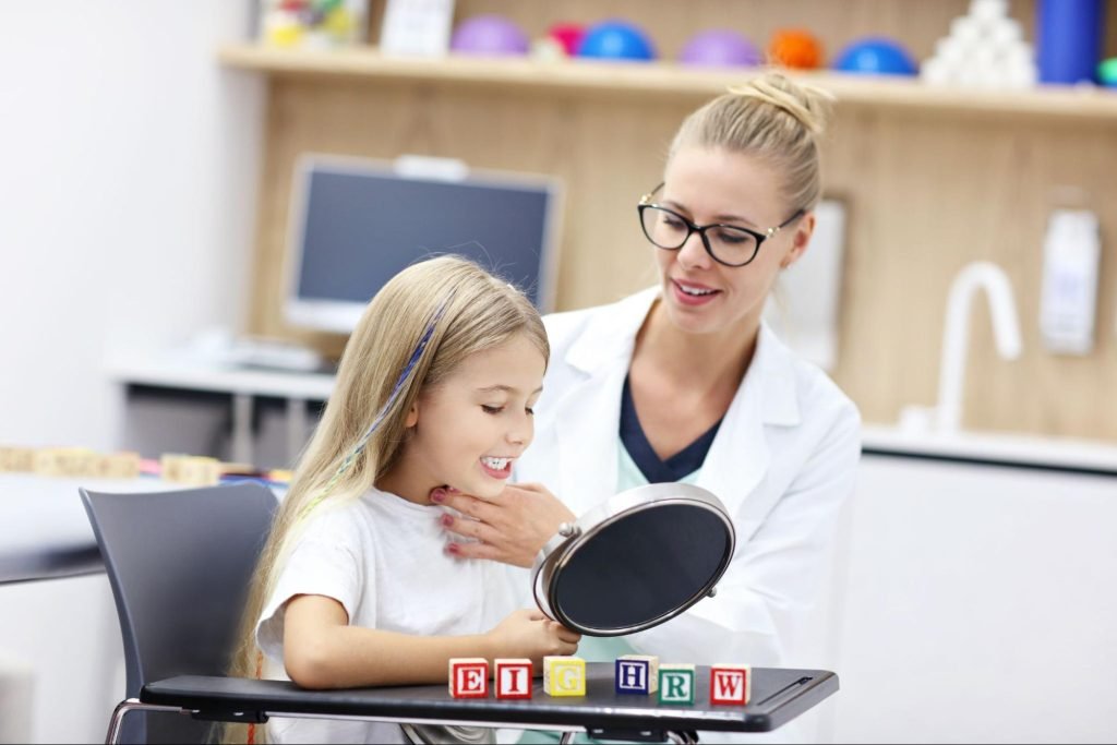 A young girl in speech therapy watches her mouth movements in a mirror during an articulation exercise.
