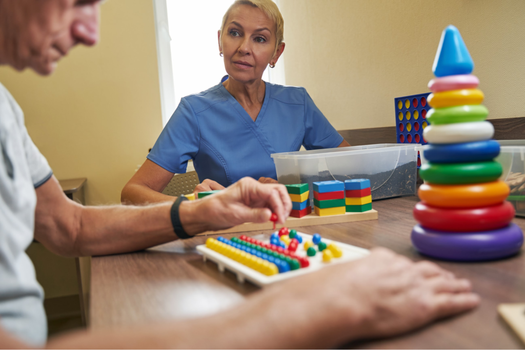 An elderly man in occupational therapy matches colored pegs to slots using rings and wooden blocks to improve motor and cognitive skills.
