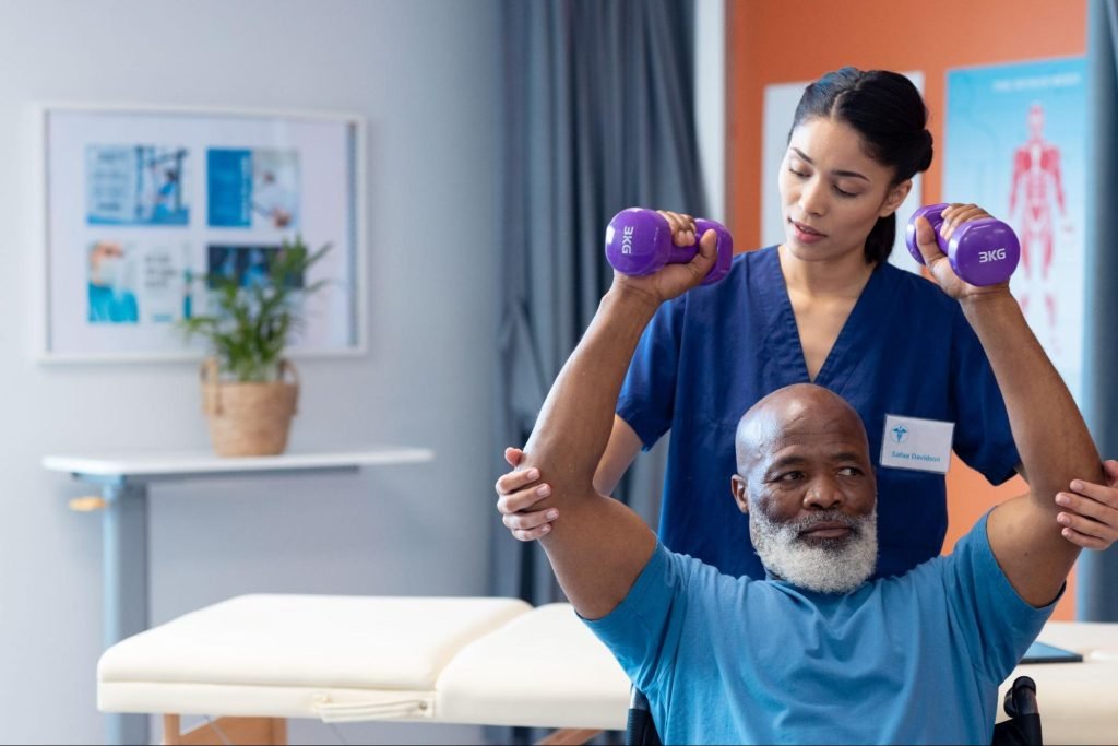 A female nurse assists an elderly African-American patient in exercising with dumbbells as part of a physical therapy routine.