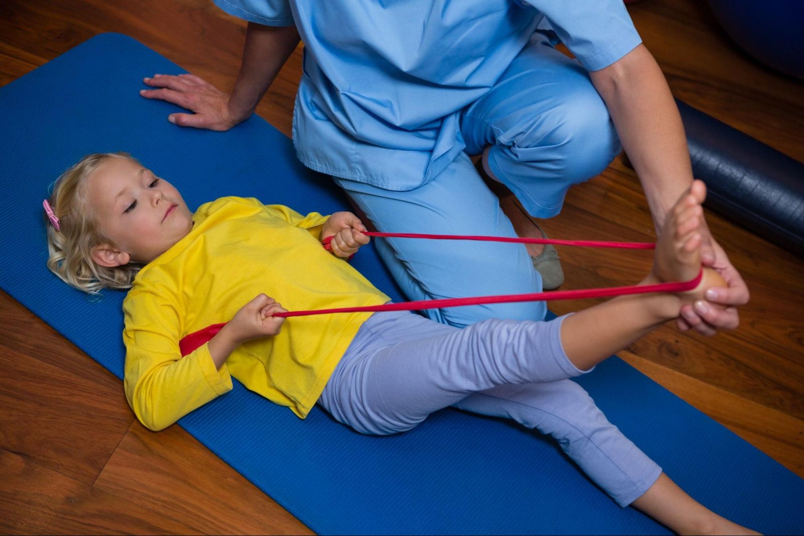 A physiotherapist guides a young girl through physical therapy exercises for injury recovery.