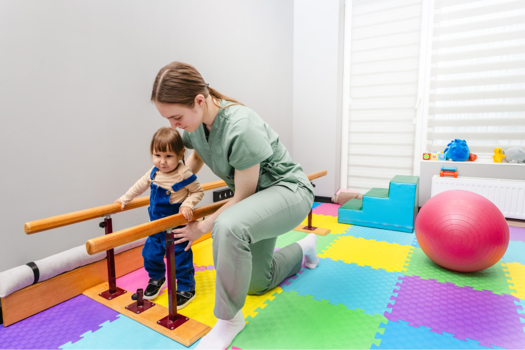 A physiotherapist helps a toddler walk using a gait training ramp.