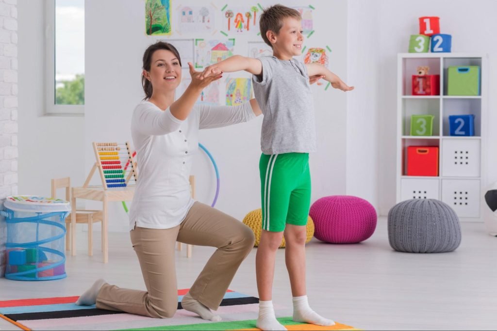 A physiotherapist works with a school-age boy to improve strength and mobility during physical therapy exercises.