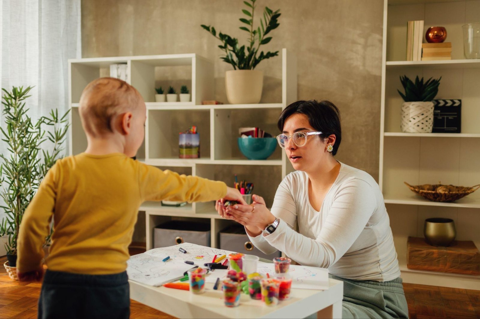A mom wearing eyeglasses plays with her son to practice communication as part of his speech therapy exercises