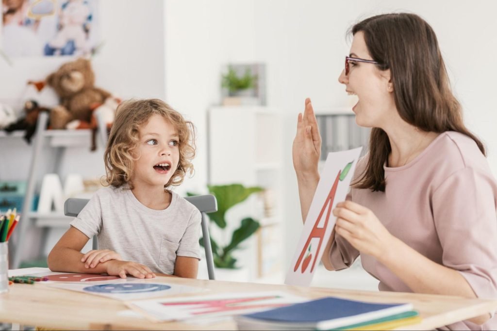 A therapist holding the letter A guides a young boy through its pronunciation during speech therapy.
