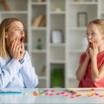A child and a therapist press their cheeks as they articulate a word together in speech and language therapy.