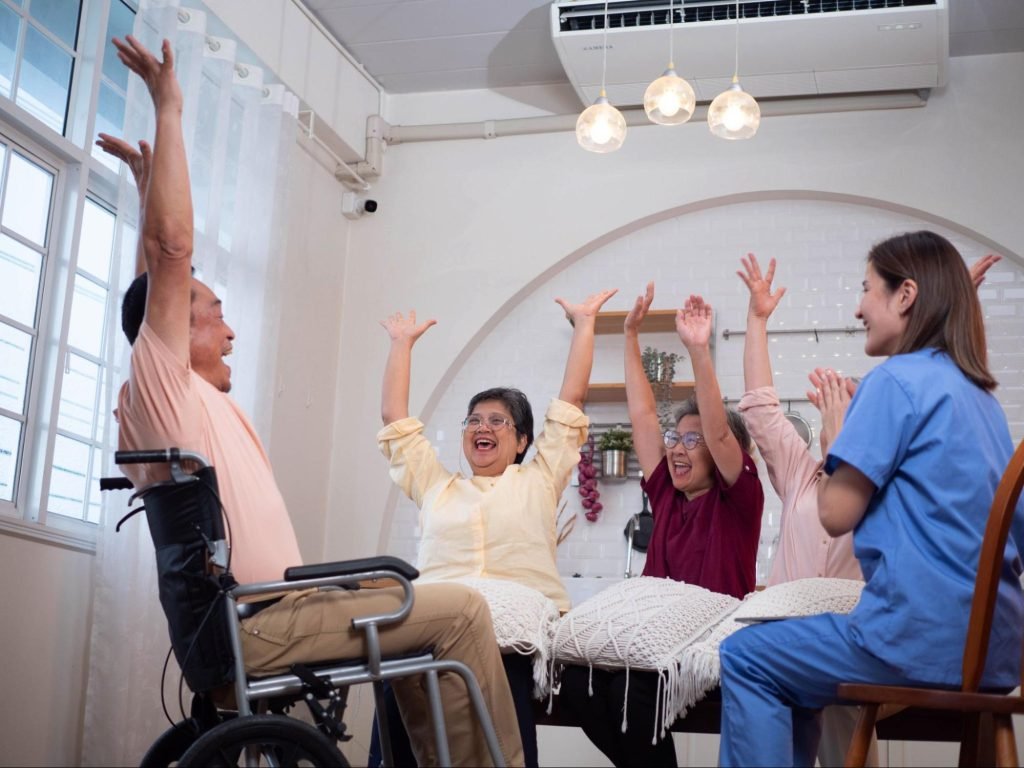 A nurse is sitting in a circle with elderly people who have their hands up in the air.