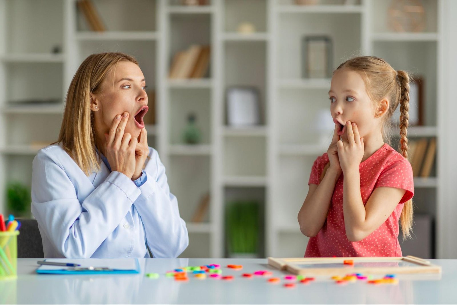 A child and a therapist press their cheeks as they articulate a word together in speech and language therapy.