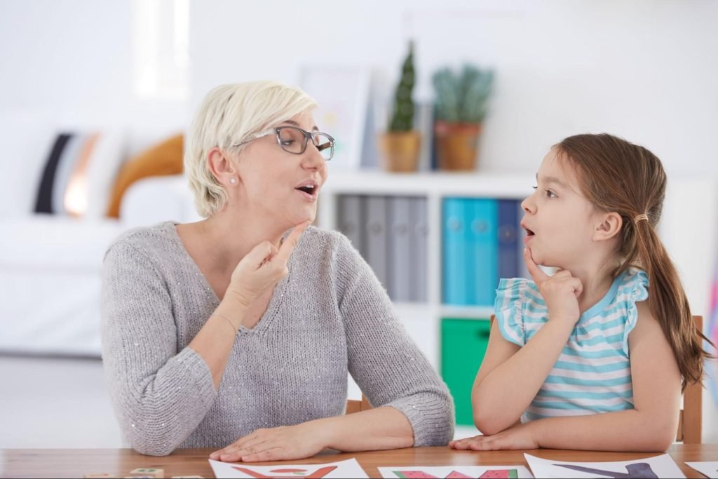 A speech therapist and a stuttering child gesture at their lips while practicing speech sounds together.