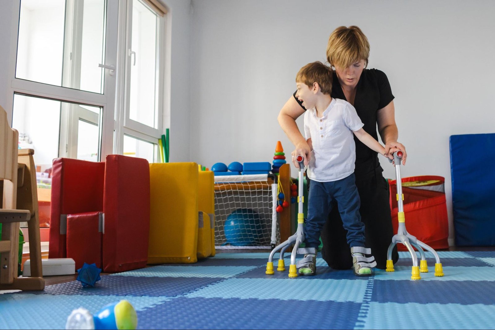 A child with cerebral palsy practices walking with support from an occupational therapist using a quad cane.