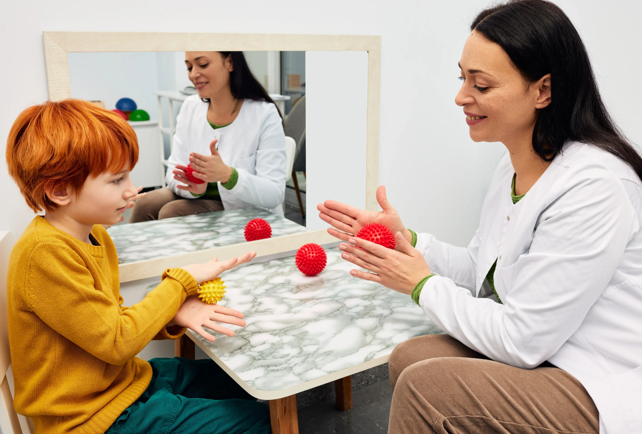 A child and his therapist roll a ball between their hands during occupational therapy.