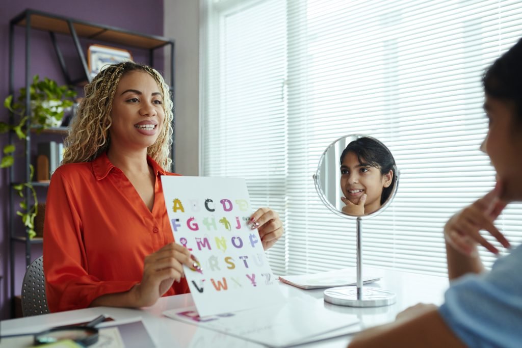 A pediatric speech therapist holds up an alphabet board to teach a young child.