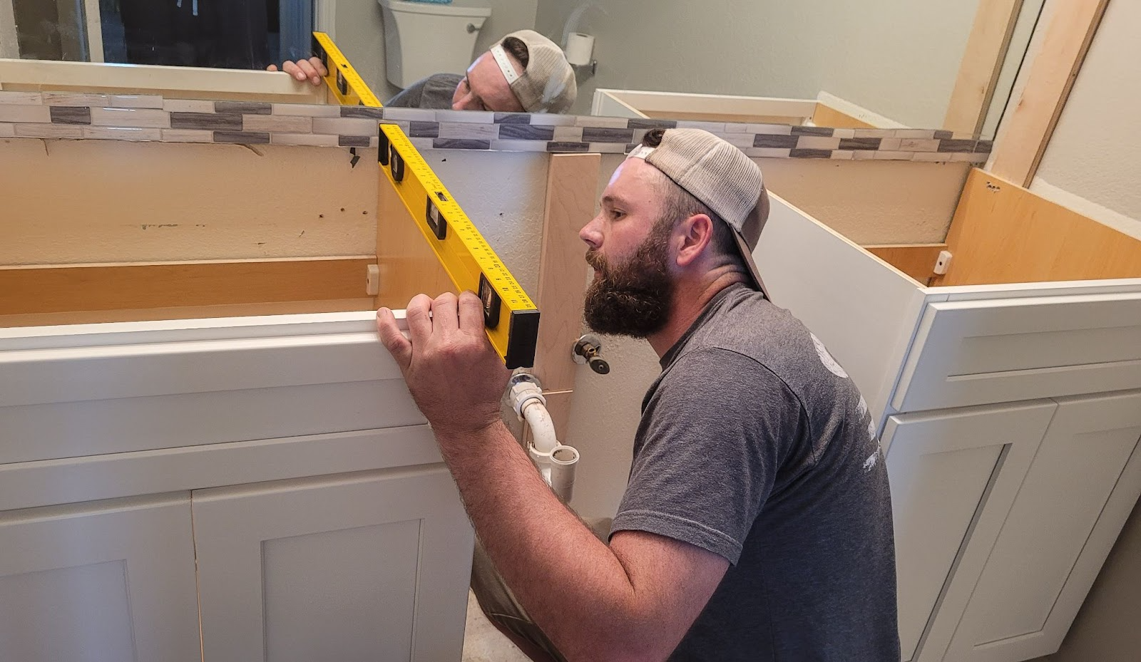 A cabinet maker checks the alignment and depth of a wooden kitchen cabinet with a level