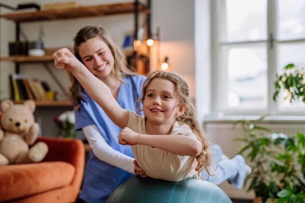 A female occupational therapist helps a young girl perform fine motor skill exercises during a session.